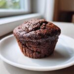 A dark, rich chocolate muffin served on a white plate, perfect alongside your Recetas de Café.