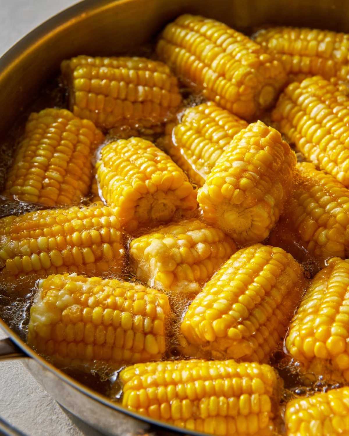 Close-up of bright yellow corn on the cob pieces simmering in a pot, illustrating how to make perfect Buttered Corn.