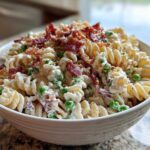A white bowl filled with creamy Crack Pasta Salad featuring rotini pasta, green peas, and topped generously with crumbled bacon.