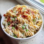 Close-up of a creamy Crack Pasta Salad featuring rotini pasta, green peas, and topped generously with crumbled bacon.