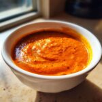 Close-up of rich, vibrant orange Creamy Garlic Tikka Masala Sauce served in a white bowl.
