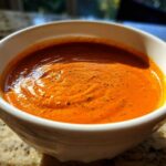 Close-up of rich, orange Creamy Garlic Tikka Masala Sauce in a white bowl, sprinkled with herbs.