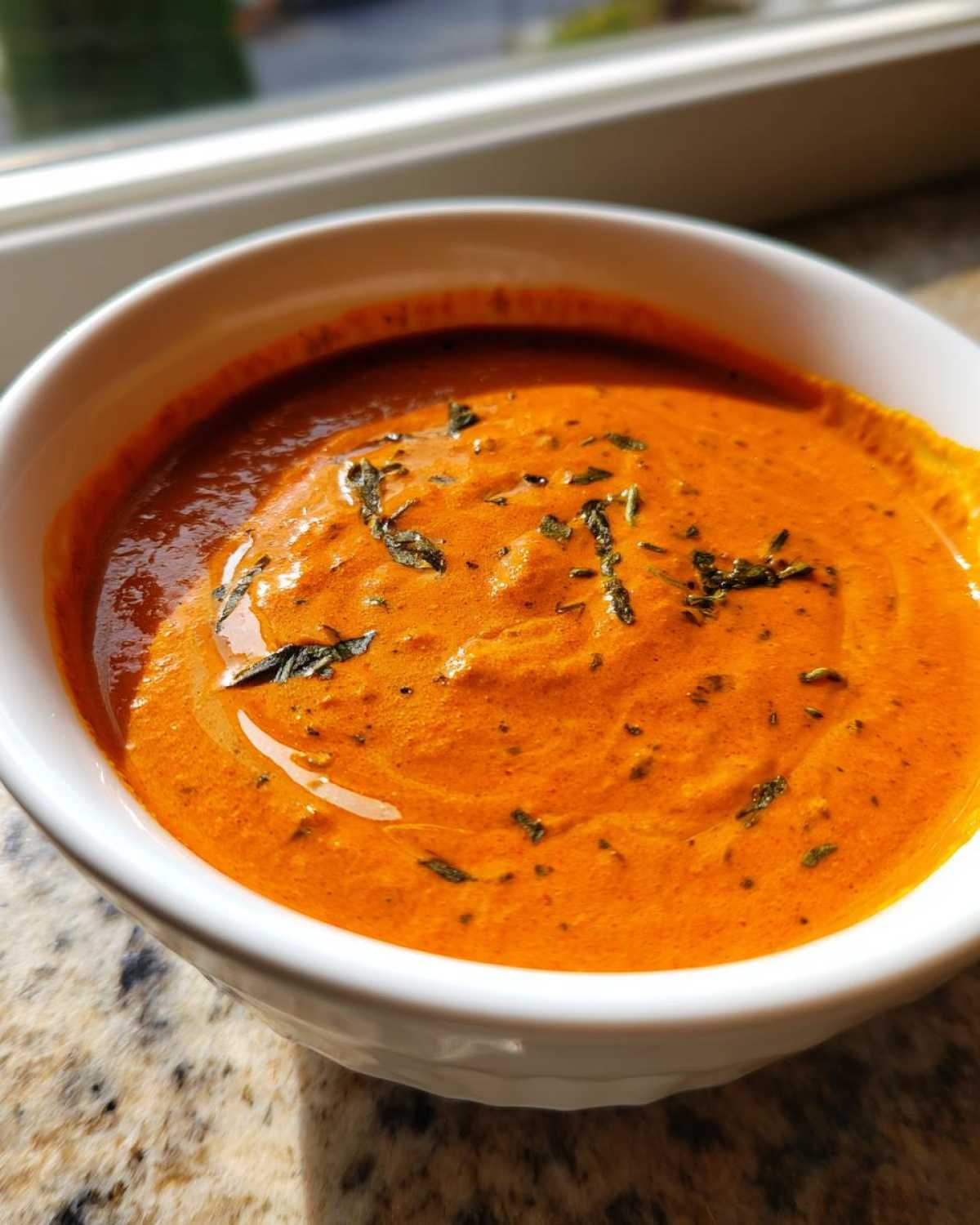 Close-up of vibrant orange Creamy Garlic Tikka Masala Sauce garnished with herbs in a white bowl.