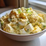 A close-up of creamy Hellman's Potato Salad mixed with chunks of hard-boiled egg and celery, topped with green onion.