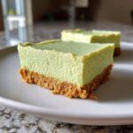 Close-up of a thick, pale green slice of Creamy Key Lime Pie Bars with a golden graham cracker crust on a white plate.