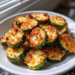 A pile of golden-brown, crispy Air Fryer Zucchini rounds topped with melted cheese and breading, served on a white plate.