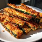 A close-up shot of golden brown Crispy Baked Parmesan Zucchini sticks piled on a white plate.