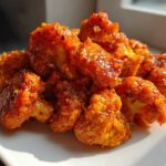 A pile of crispy, orange-glazed Bang Bang Cauliflower florets glistening on a white square plate.