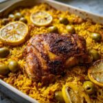 Close-up of a Crispy One Pan Portuguese Chicken and Rice Bake with golden chicken, yellow rice, green olives, and roasted lemon slices.