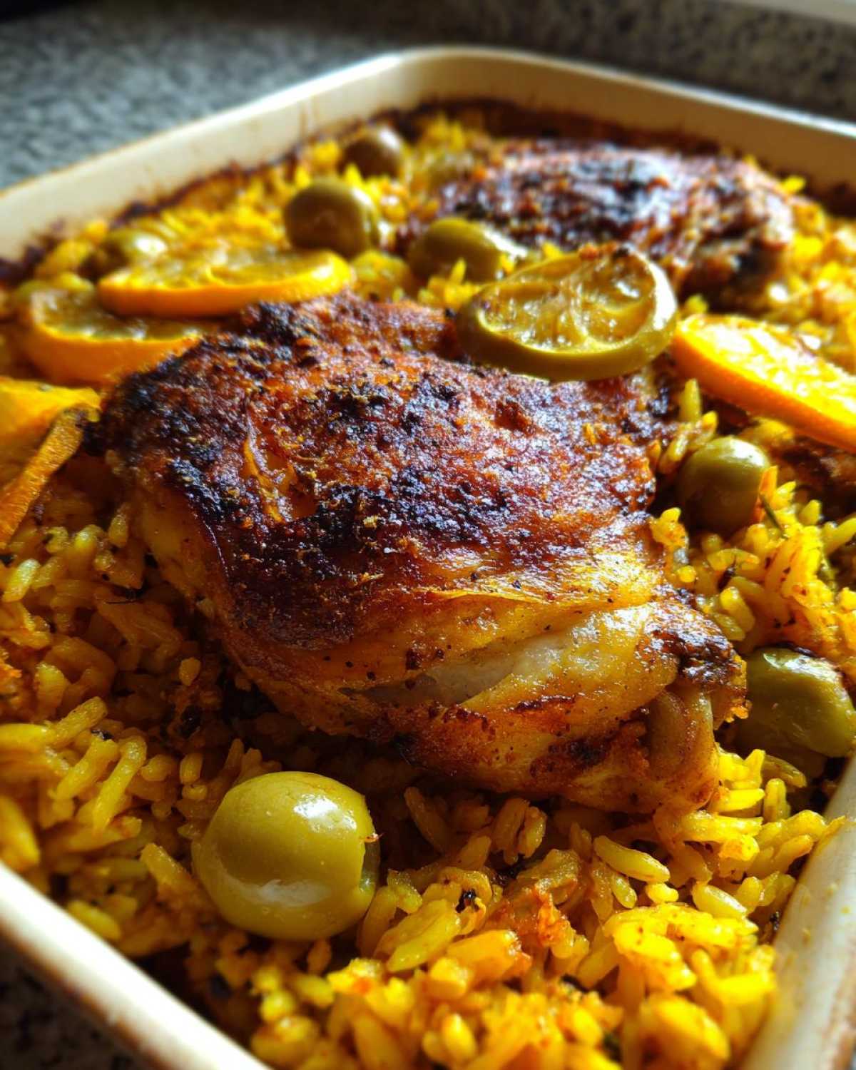 Close-up of crispy skin on a chicken thigh baked over yellow rice with olives in a one pan Portuguese Chicken and Rice Bake.