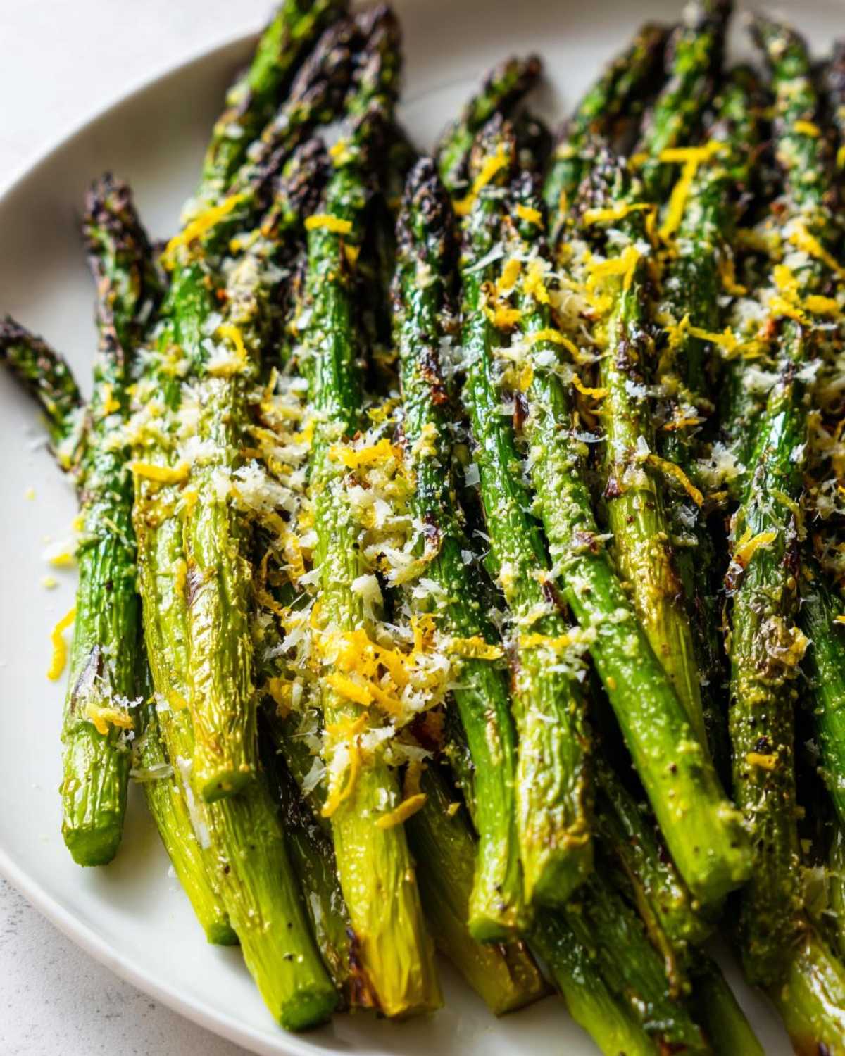 Close-up of bright green, crispy roasted asparagus topped with grated Parmesan cheese and lemon zest.
