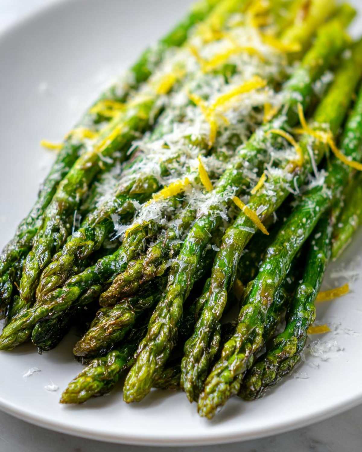 Close-up of Crispy Roasted Asparagus topped with grated Parmesan cheese and bright lemon zest on a white plate.
