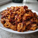 A close-up shot of shredded, caramelized Crispy Slow Cooker Carnitas piled high on a white serving dish.