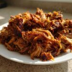A generous mound of golden brown, shredded, crispy slow cooker carnitas piled high on a white plate.