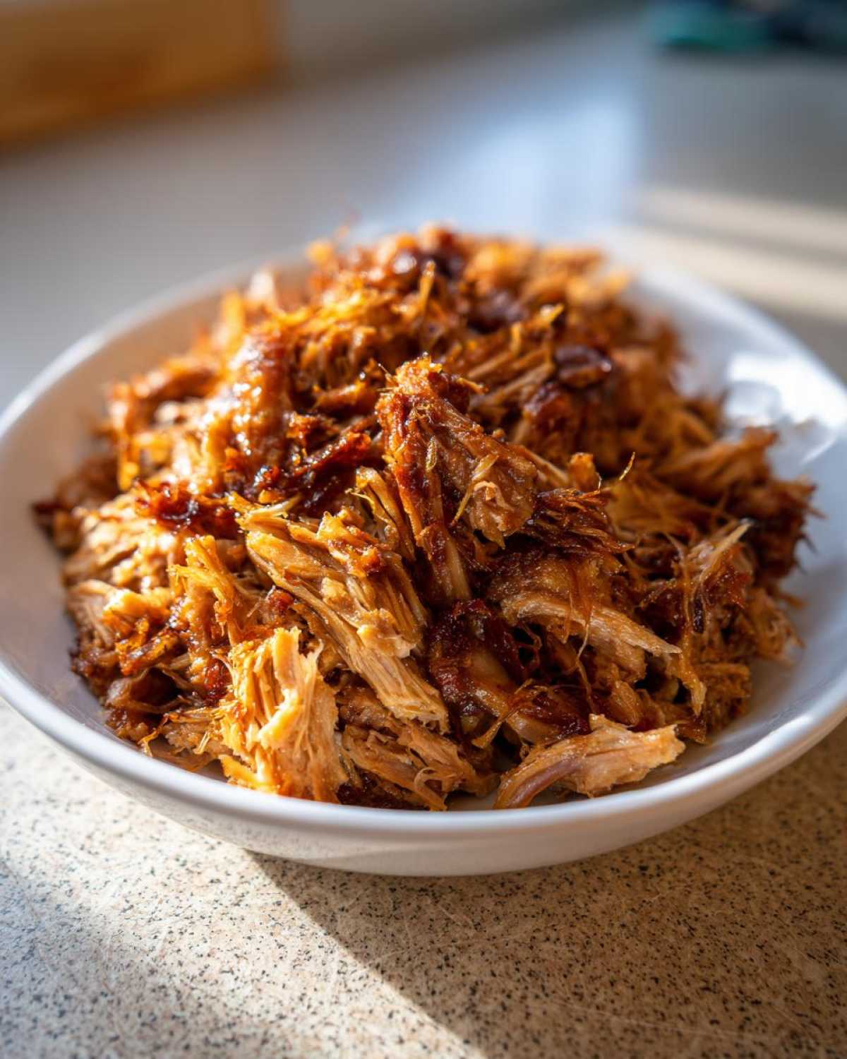 A close-up of shredded, crispy Slow Cooker Carnitas piled high in a white bowl.