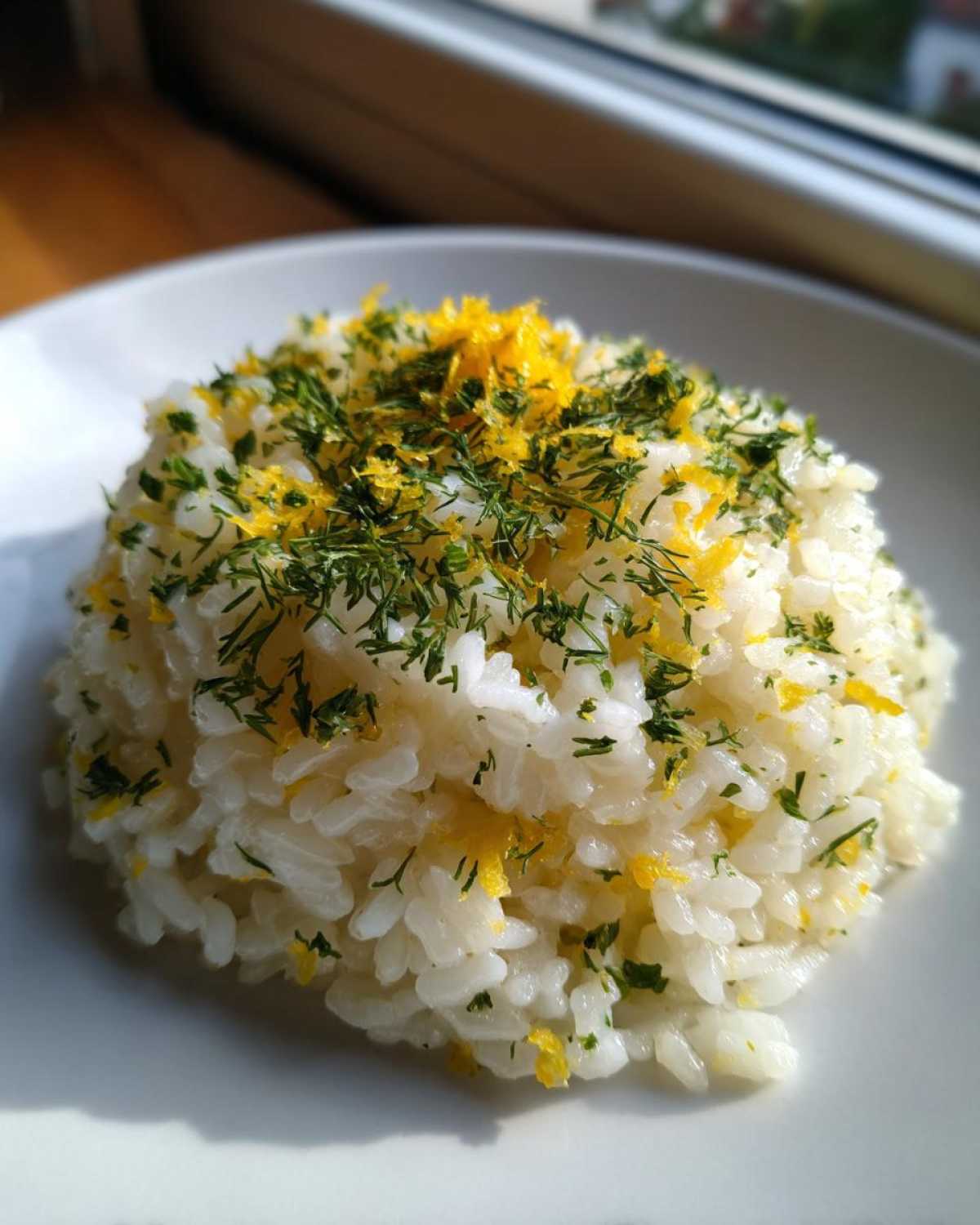 A mound of fluffy Greek Lemon Rice topped generously with bright yellow lemon zest and fresh green dill.