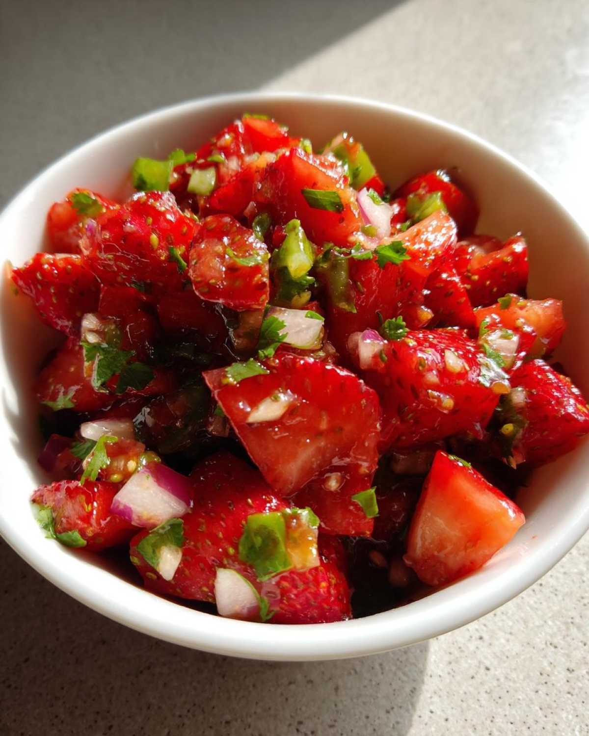 Close-up of vibrant, chunky Strawberry Salsa featuring diced strawberries, red onion, and cilantro in a white bowl.