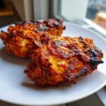 Two juicy Garam Masala Chicken Thighs with a rich, reddish-orange spice crust resting on a white plate.