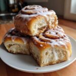 Three fluffy, freshly baked Breakfast Rolls stacked on a white plate, drizzled generously with white icing.