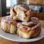 A stack of three gooey, iced Breakfast Rolls with one piece broken open to show the soft interior.