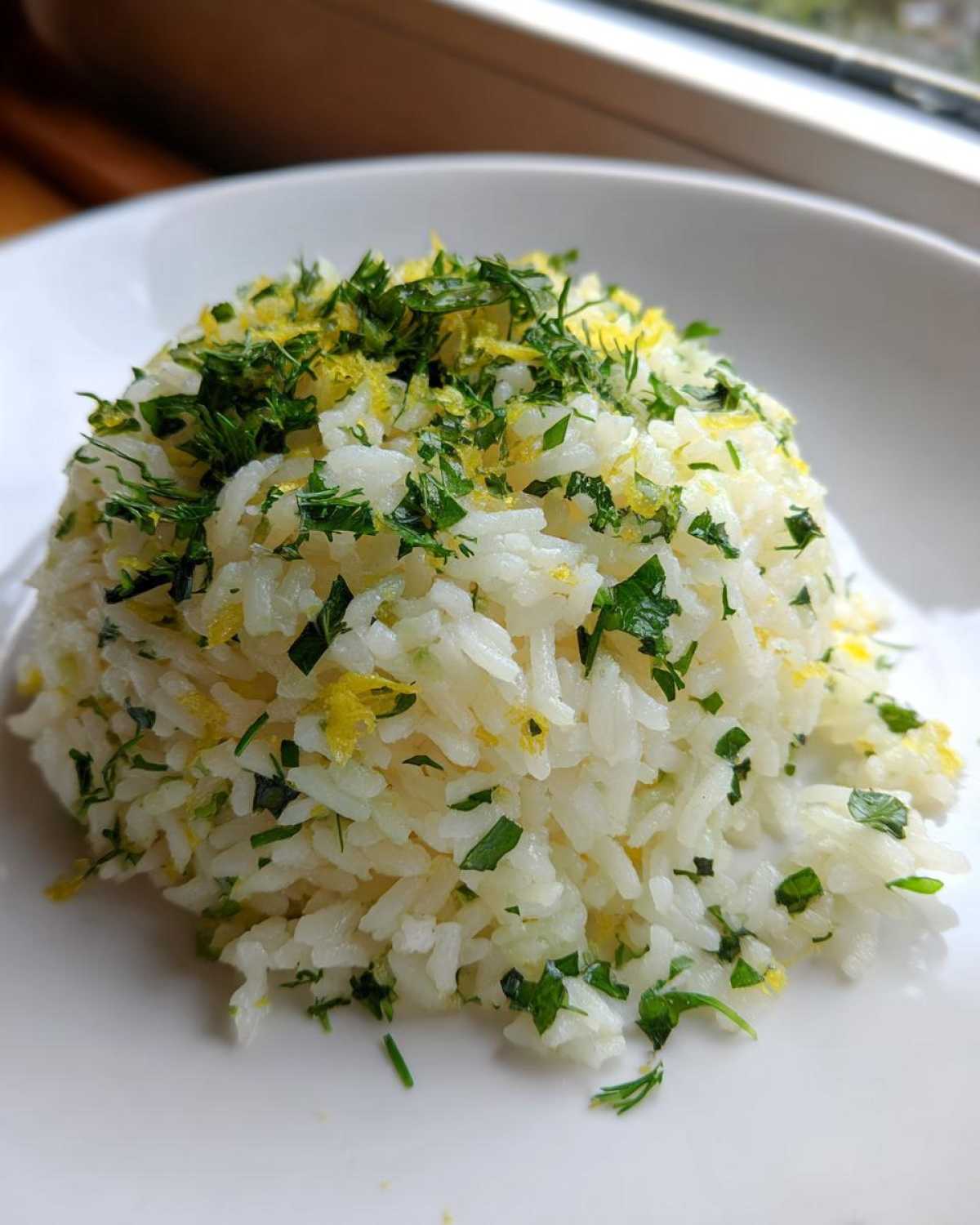 A mound of fluffy Greek Lemon Rice topped generously with fresh parsley, dill, and bright yellow lemon zest.