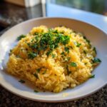 A white bowl filled with bright yellow Greek Lemon Rice, topped generously with fresh chopped parsley.