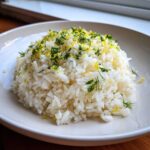 A mound of fluffy Greek Lemon Rice garnished generously with bright yellow lemon zest and chopped fresh dill.