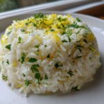 A mound of fluffy Greek Lemon Rice topped with bright yellow lemon zest and fresh chopped parsley on a white plate.