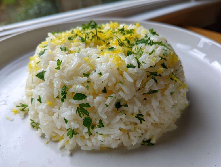 A mound of fluffy Greek Lemon Rice topped with bright yellow lemon zest and fresh chopped parsley on a white plate.