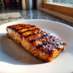 A perfectly cooked fillet of Grilled Honey Mustard Salmon with visible grill marks and a shiny glaze on a white plate.
