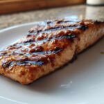 A perfectly cooked fillet of Grilled Honey Mustard Salmon with visible grill marks and a glossy glaze, served on a white plate.