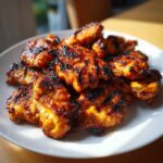 Close-up of several pieces of juicy, charred Grilled Vietnamese Chicken piled on a white plate.