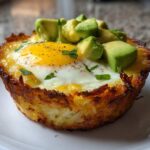 Close-up of a single, crispy Hash Brown Avocado Egg Cup with a baked egg and diced avocado topping.
