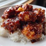 Close-up of crispy Hawaiian Chicken pieces coated in a dark, glossy sauce served over fluffy white coconut rice.