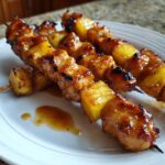 Close-up of three glistening Hawaiian Teriyaki Chicken Kabobs Pineapple skewers resting on a white plate with extra glaze.