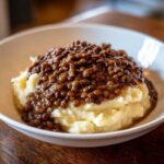 A close-up of Hearty Lentil Stew with Creamy Mashed Potatoes served in a white bowl on a wooden table.