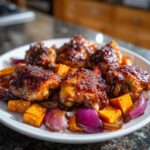 Close-up of sticky, glazed Honey Harissa Chicken pieces served over roasted sweet potatoes and red onions.