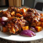 Close-up of glazed Honey Harissa Chicken pieces served with roasted sweet potatoes and red onion wedges on a white plate.