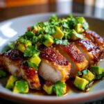 Close-up of sliced, glazed chicken breast topped with diced avocado and fresh cilantro for the Honey Lime Chicken Avocado Meal.