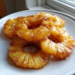 Close-up of several glistening Honey Lime Roasted Pineapple rings stacked on a white plate.
