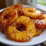 A close-up of several glistening, caramelized rings of Honey Lime Roasted Pineapple served on a white plate.
