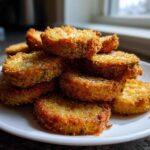 A stack of golden brown, Impossibly Crispy Baked Eggplant slices seasoned with salt on a white plate.