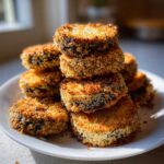 A stack of golden brown, breaded, and Impossibly Crispy Baked Eggplant slices on a white plate.