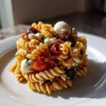 A molded serving of Italian Pasta Salad featuring fusilli pasta, cherry tomatoes, mozzarella balls, and olives on a white plate.