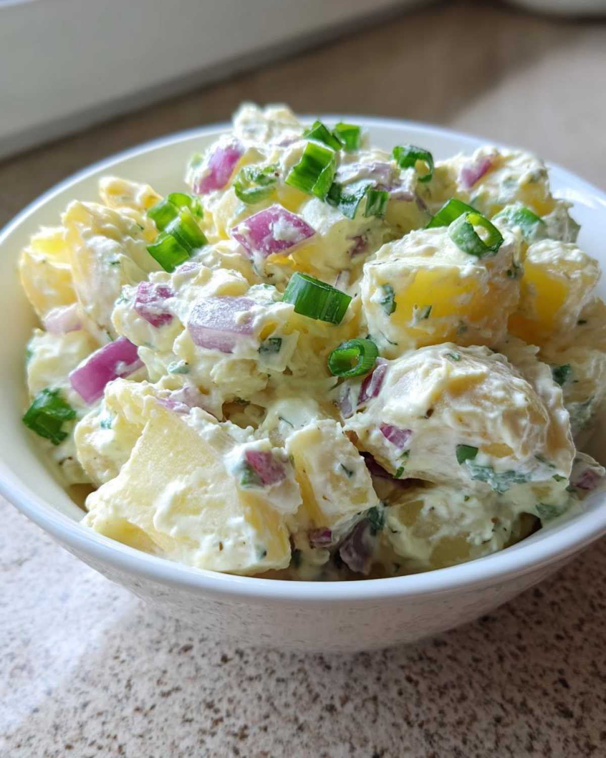 Close-up of creamy Jamaican Jerk Potato Salad mixed with red onion and topped with fresh green onions.