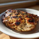 A perfectly cooked piece of Grilled Cuban Chicken breast with visible grill marks and herbs on a white plate.
