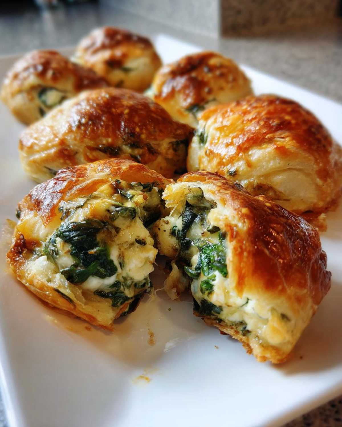 Close-up of golden brown Knapperige Spinazie Bites met Feta en Gesmolten Kaas, one is broken open showing the spinach and cheese filling.