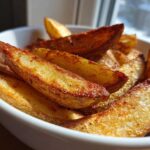 Close-up of crispy, golden brown Lemon Greek Potatoes wedges served in a white bowl.