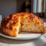 A freshly baked loaf of No Knead Cheddar Bread in Dutch Oven, cut open to show the airy crumb and melted cheese.