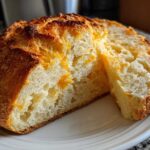 A rustic loaf of No Knead Cheddar Bread in Dutch Oven, sliced open to show the cheesy interior and golden crust.